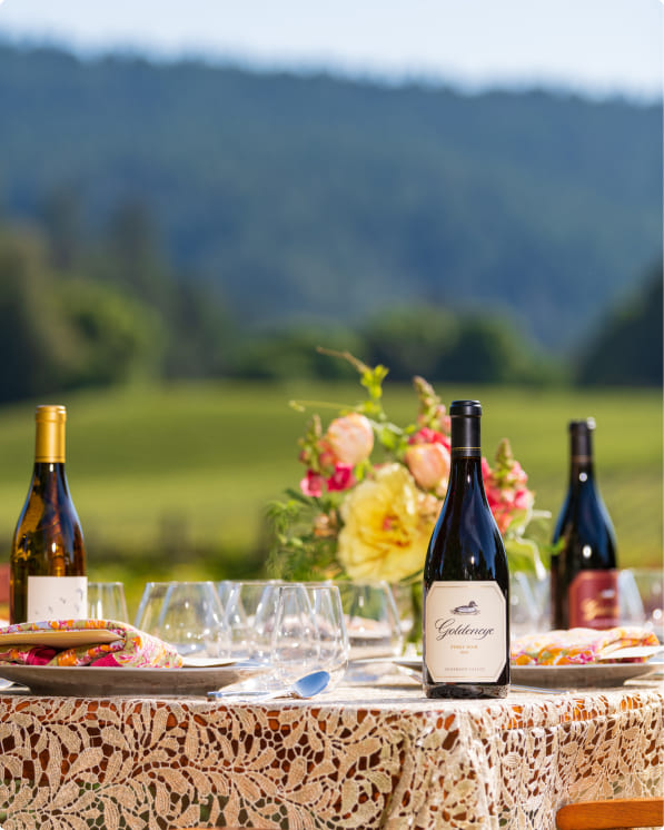 Wine bottles and table setting arranged outdoors with vineyard views